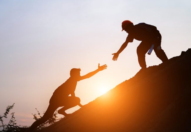 Tourists go up the hill in the sunrise to shake hands The male traveler shakes the hand of the male traveler who is climbing to the top of the hill